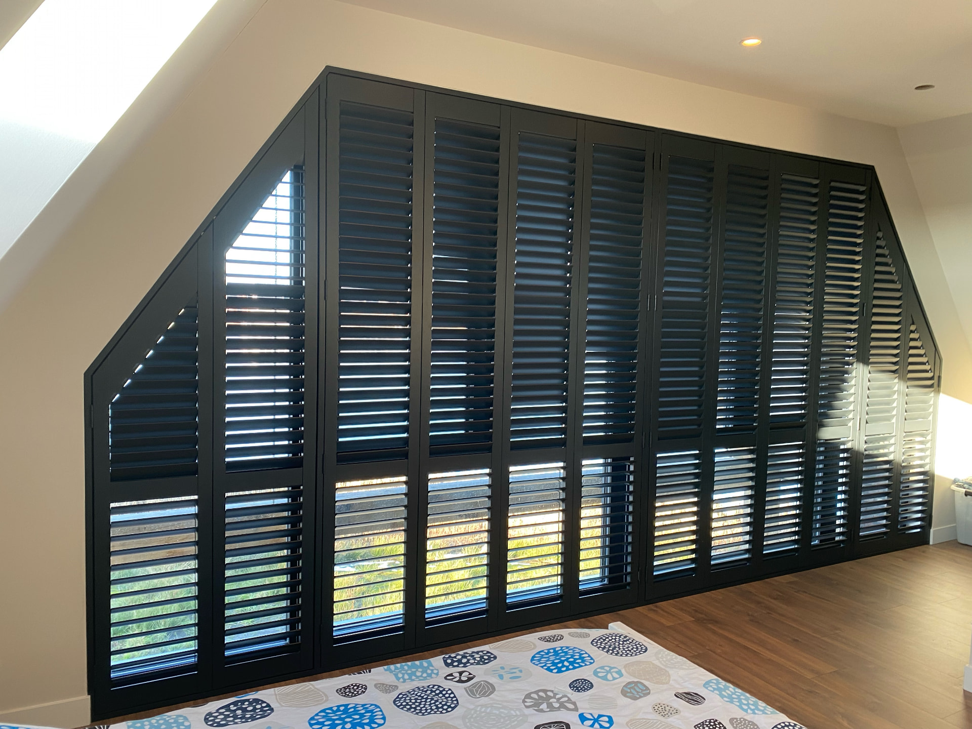 Antracietkleurige shutters over de volle breedte van een slaapkamer met schuin dak